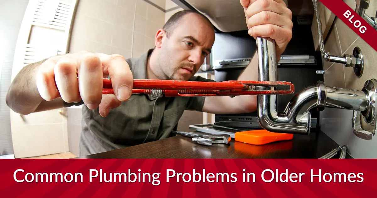 A plumber fixing under-sink pipes with a wrench.